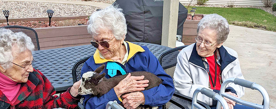 Senior ladies hold and pet a baby goat brought in by a staff member.